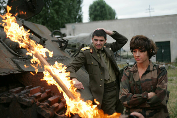 Two people look at a burning tank, still from I DO NOT CARE IF WE GO DOWN IN HISTORY AS BARBARIANS