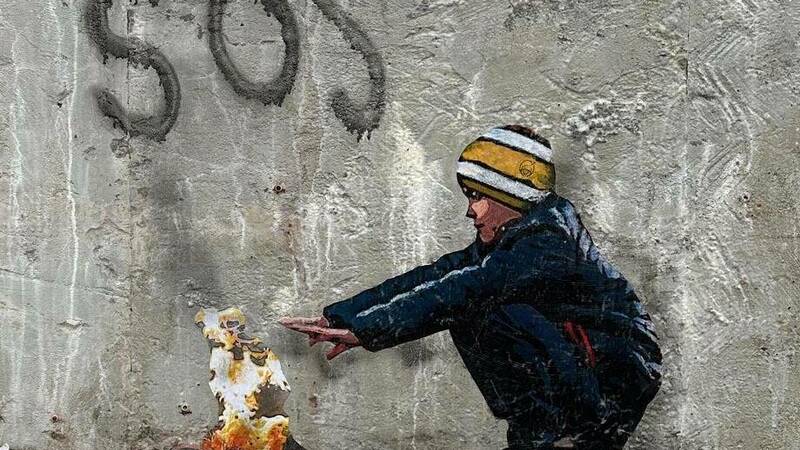 SOS. Street art of boy warming hands over fire.
