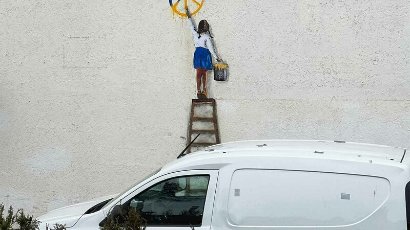 Mural of girl/young woman painting a peace symbol in Ukrainian colors.