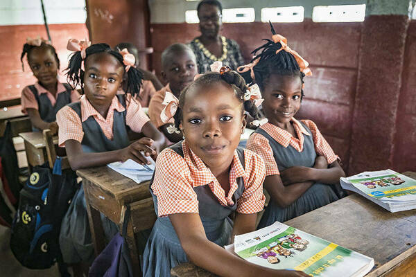 A classroom of Haitian elementary students with a teacher, all sitting at their desks with books in front of them