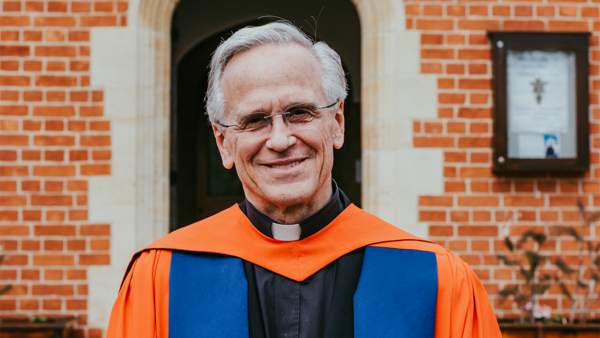 Former Notre Dame President Rev. John I. Jenkins, C.S.C., smiling in a blue and orange robe.