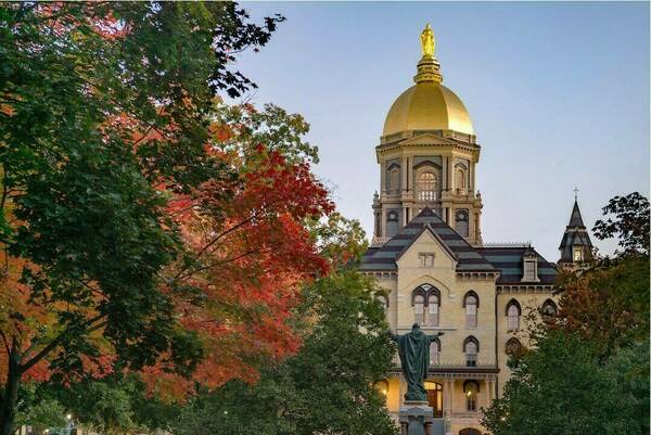 Notre Dame's Main Building, foregrounded by autumn trees and the statue of Jesus Christ and His Sacred Heart.