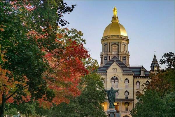 Notre Dame's Main Building, foregrounded by autumn trees and the statue of Jesus Christ and His Sacred Heart.