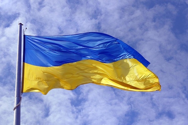 The flag of Ukraine flying against a bright, partly cloudy sky.