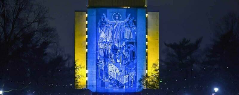The Hesburgh Memorial Library at the University of Notre Dame, pictured at night. The Word of Life mural, depicting religious iconography, including most prominently Jesus with his arms open wide, is illuminated with the yellow and blue colors of the Ukrainian flag.