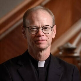 Head shot of Rev. Robert A. Dowd, C.S.C. He is wearing a black suit and clerical collar and wearing glasses.