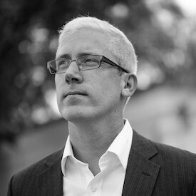 Greyscale headshot of Rory Finnin, who is looking off into the distance. He is wearing glasses and a blazer.