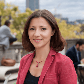 Outdoors headshot of Olesya Khromeychuk, who is wearing a red necklace, a black top, and a red blazer.