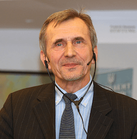 Headshot of Mykola Riabchuk, who is wearing an audio earpiece, a suit, and a tie.