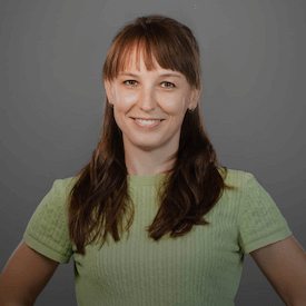 Headshot of Olena Kovalenko, who is wearing a green shirt and standing in front of a grey backdrop.