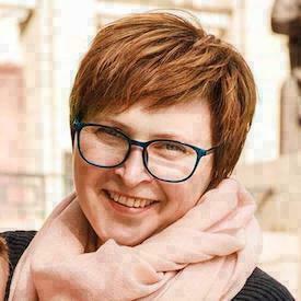 Outdoors headshot of Olga Filippova, who is wearing blue glasses and a pink neck-scarf.