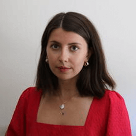 Headshot of Anna Bisikalo, who is wearing a white necklace, small gold hoop earrings, and a red blouse.