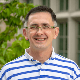 Outdoors headshot of Volodymyr Turchynovskyy, who is wearing thinly framed glasses and a striped blue polo shirt.