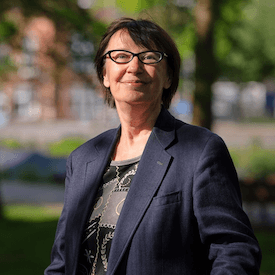 Outdoors headshot of Natalka Bilotserkivets, who is wearing a grey shirt, navy blazer, and black-framed glasses.