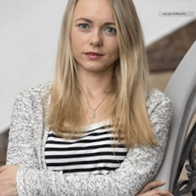 Headshot of Olha Tkachenko, who is wearing a black/white striped shirt underneath a grey sweater.