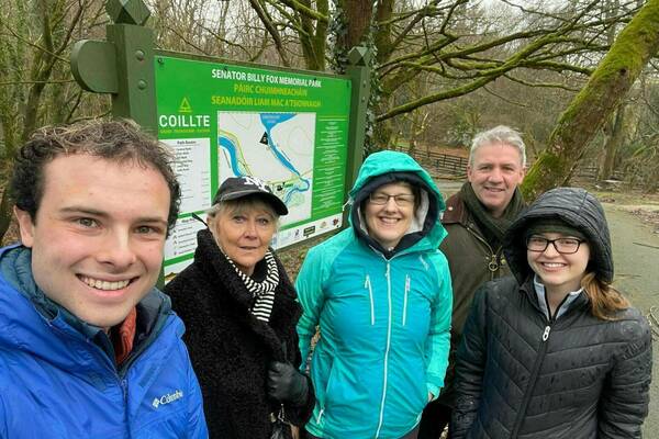 Five smiling people stand in front of a green sign for Senator Billy Fox Memorial Park. The sign includes a map of the park's trails. The people are dressed in jackets appropriate for cool, potentially wet weather.