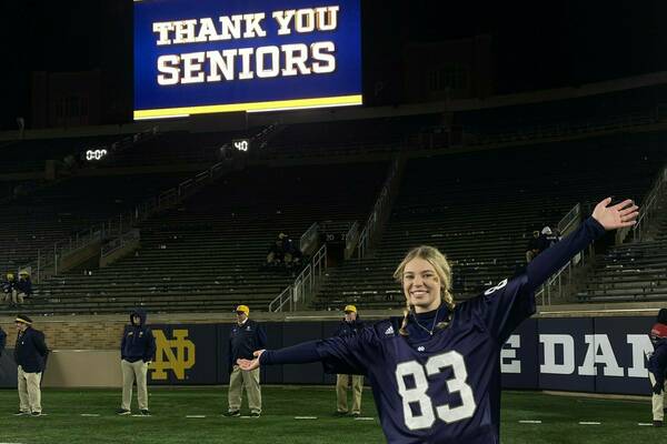 A female student wearing a football jersey poses in front of a sign that reads, "Thank you seniors."