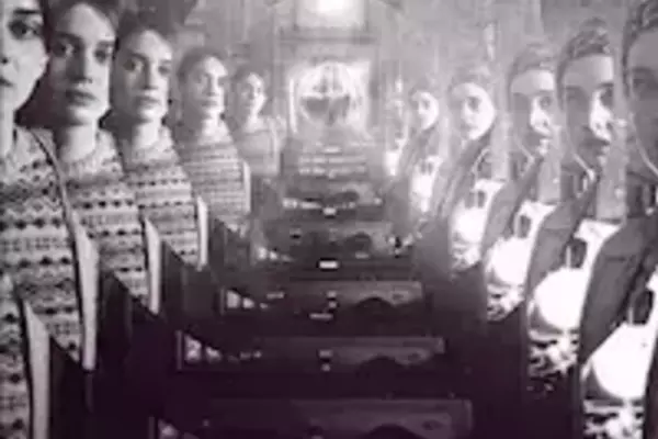 Multiple women with serious expressions look forward, flanking a dark, arched hall with steps leading to a distant light. They wear dark, patterned clothing. The title 'LOLA' appears in bright yellow at the bottom.