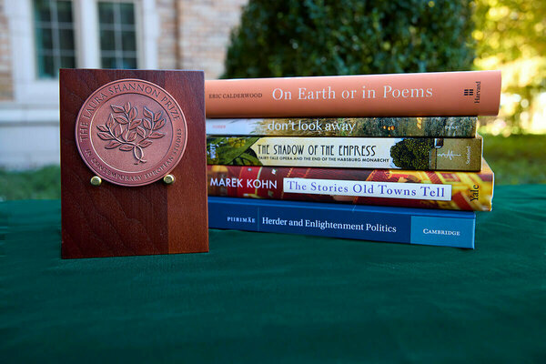 A wooden plaque with a copper medal for "The Laura Shannon Prize in Contemporary European Studies" stands next to a stack of five academic books on a green tablecloth outdoors.