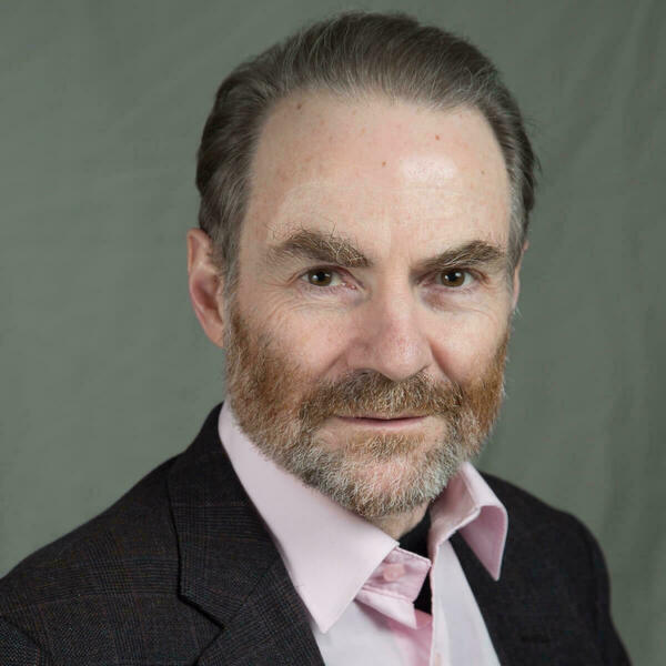 Timothy Garton Ash with grey hair and brown beard, wearing a dark suit jacket and light pink shirt, with a gentle expression.