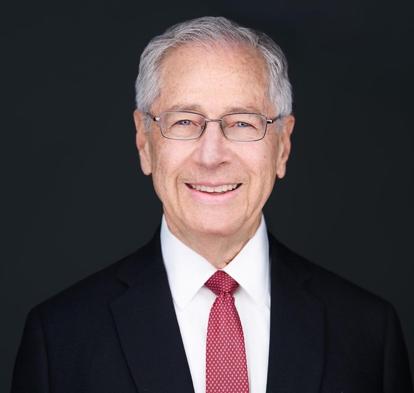 Mark Gitenstein smiles wearing glasses, a black suit, white shirt, and a red tie.